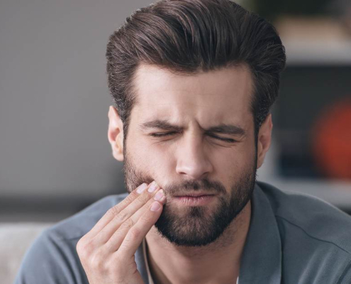 A man in pain due to a severe toothache, holding his cheek with one hand.