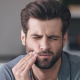 A man in pain due to a severe toothache, holding his cheek with one hand.