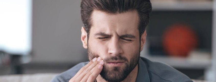 A man in pain due to a severe toothache, holding his cheek with one hand.