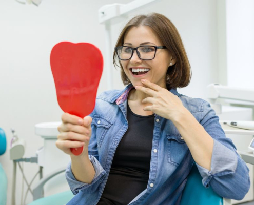 Patient smiling while viewing new fixed full arch implants in a dental clinic mirror