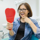 Patient smiling while viewing new fixed full arch implants in a dental clinic mirror