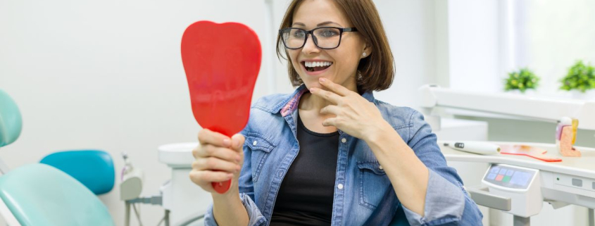 Patient smiling while viewing new fixed full arch implants in a dental clinic mirror